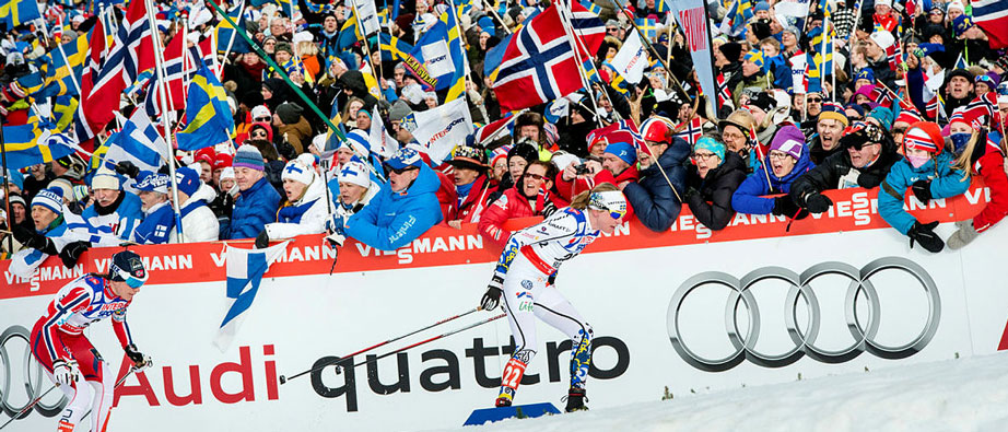 Svensk skidåkare framför publik med svenska och norska flaggor