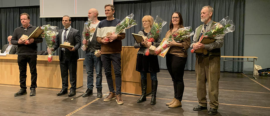 Sju personer står på en scen med blommor i famnen
