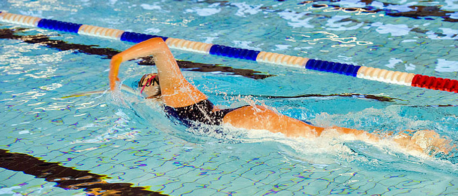 Kvinna iförs svart baddräkt som, simmar frisim i bassäng