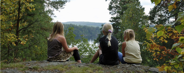 Tre barn sitter på en bergsknalle ( Adriansberg ) och blickar ut över Runn och skog