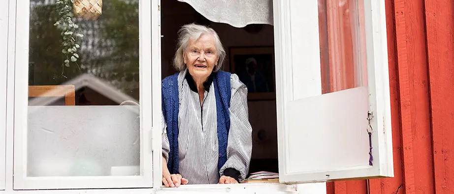 Äldre dam som tittar ut genom ett öppet fönster