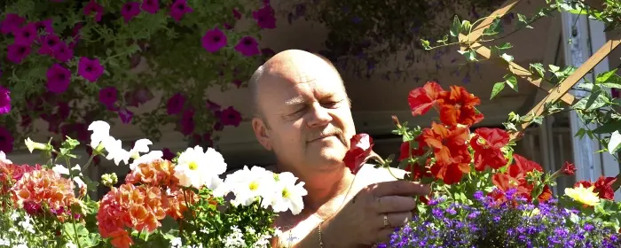 En man som står och påtar med blommor i en blomlåda