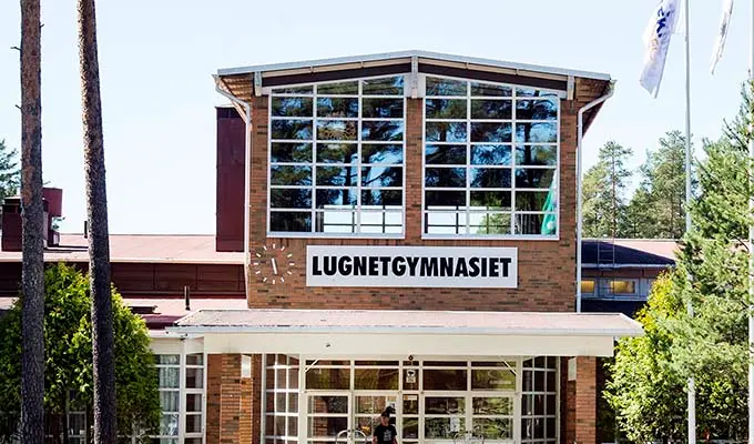 Vy över Lugnetgymnasiets fasad med klocka och skolans namn.
