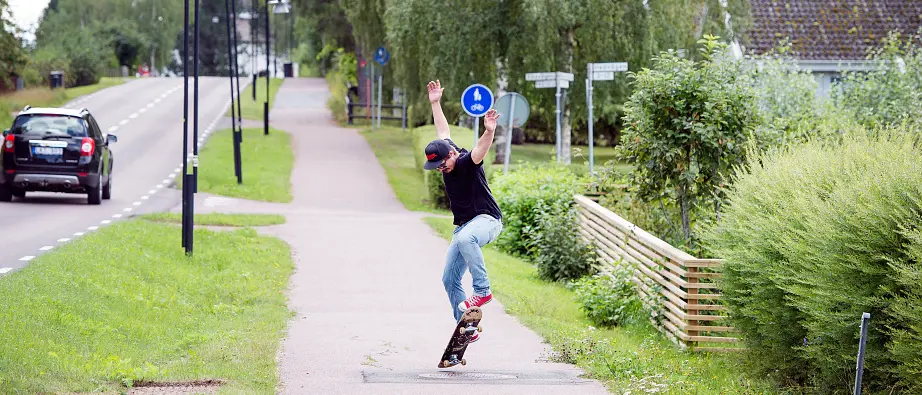 En kille gör ett trick på en skateboard på en cykelbana som går parallellt med en väg och brevid ett bostadsområde