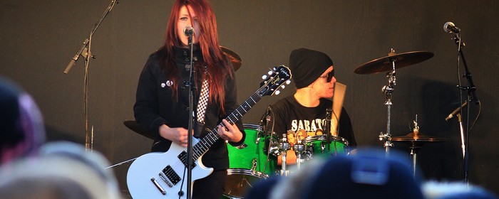 En tjej i rött hår sjunger och spelar elgitarr tillsammans med en kille i mössa och glasögon som spelar trummor