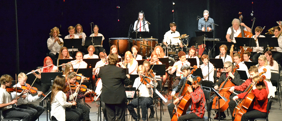 Flera ungdomar sitter på en scen och spelar i en orkester