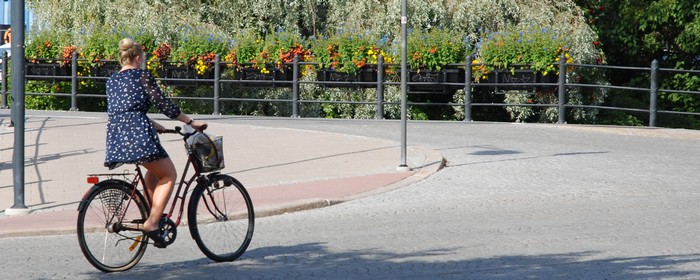 En tjej i blommig klänning cyklar på gatstensgata