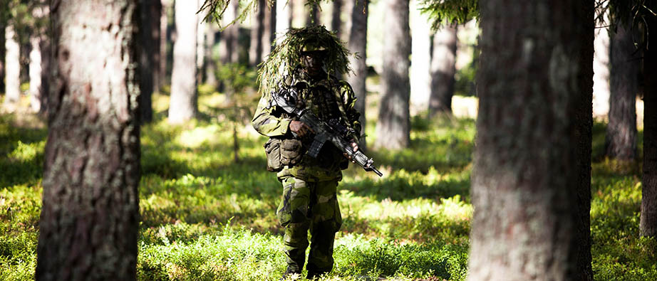 Kamouflagemålad militär i stridsmundering är ute i skogen