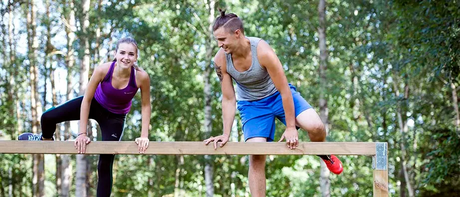 En tjej och en kille i träningskläder som klättrar över ett hinder