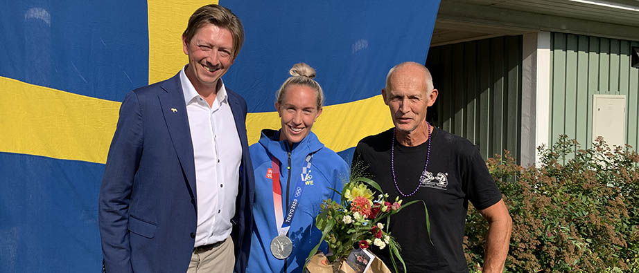Pristagaren tillsammans med två andra personer framför en svensk flagga