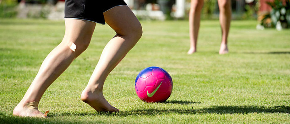 Fötter som sparkar en fotboll på grön plan.