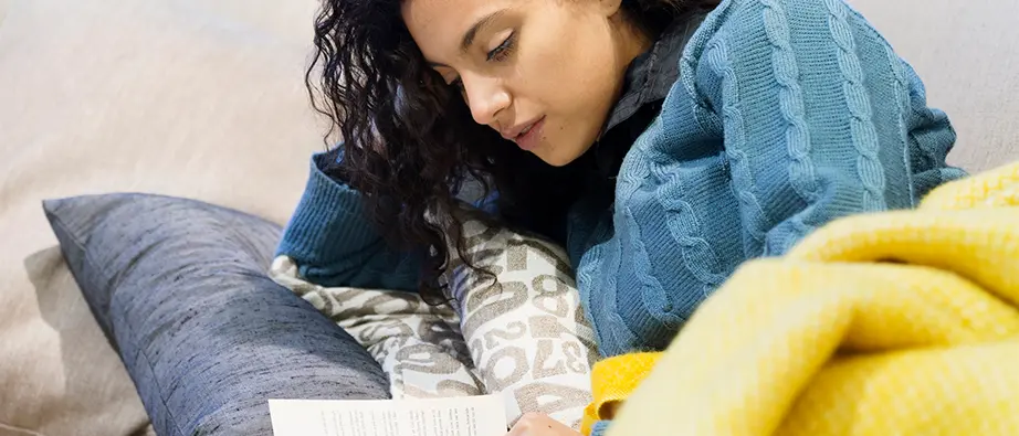 En tjej som ligger i en säng och läser en bok